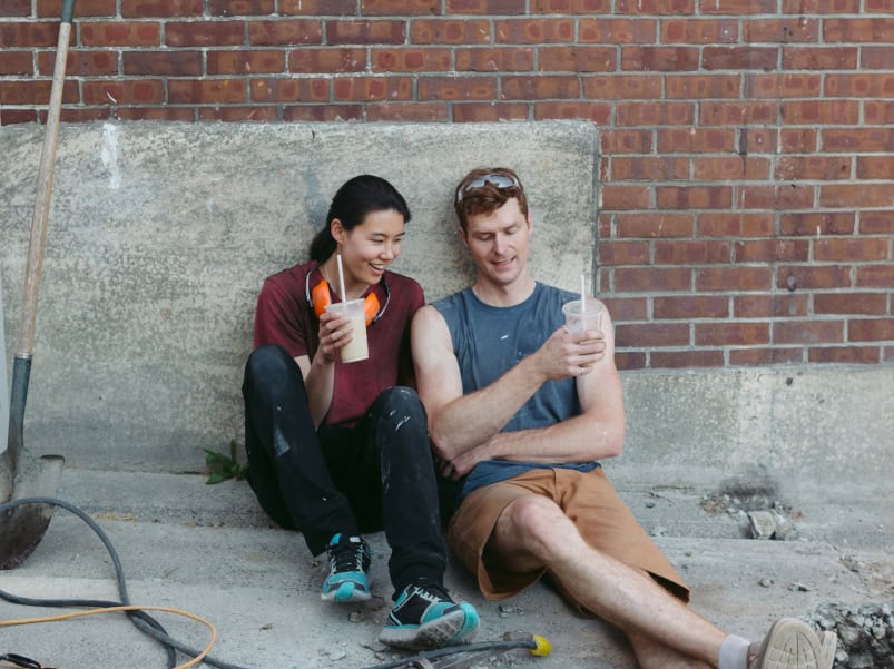 two people sitting down on the ground with their drinks