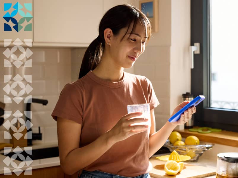 woman smiling while holding a cup and looking at her mobile phone
